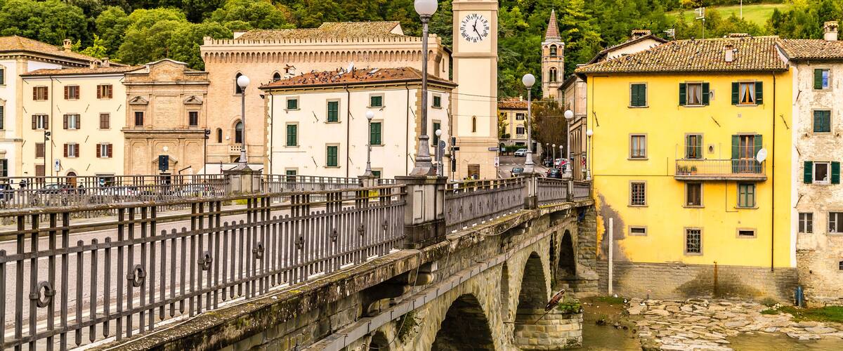 A stone bridge with arches, a clock tower, and buildings with traditional architecture.