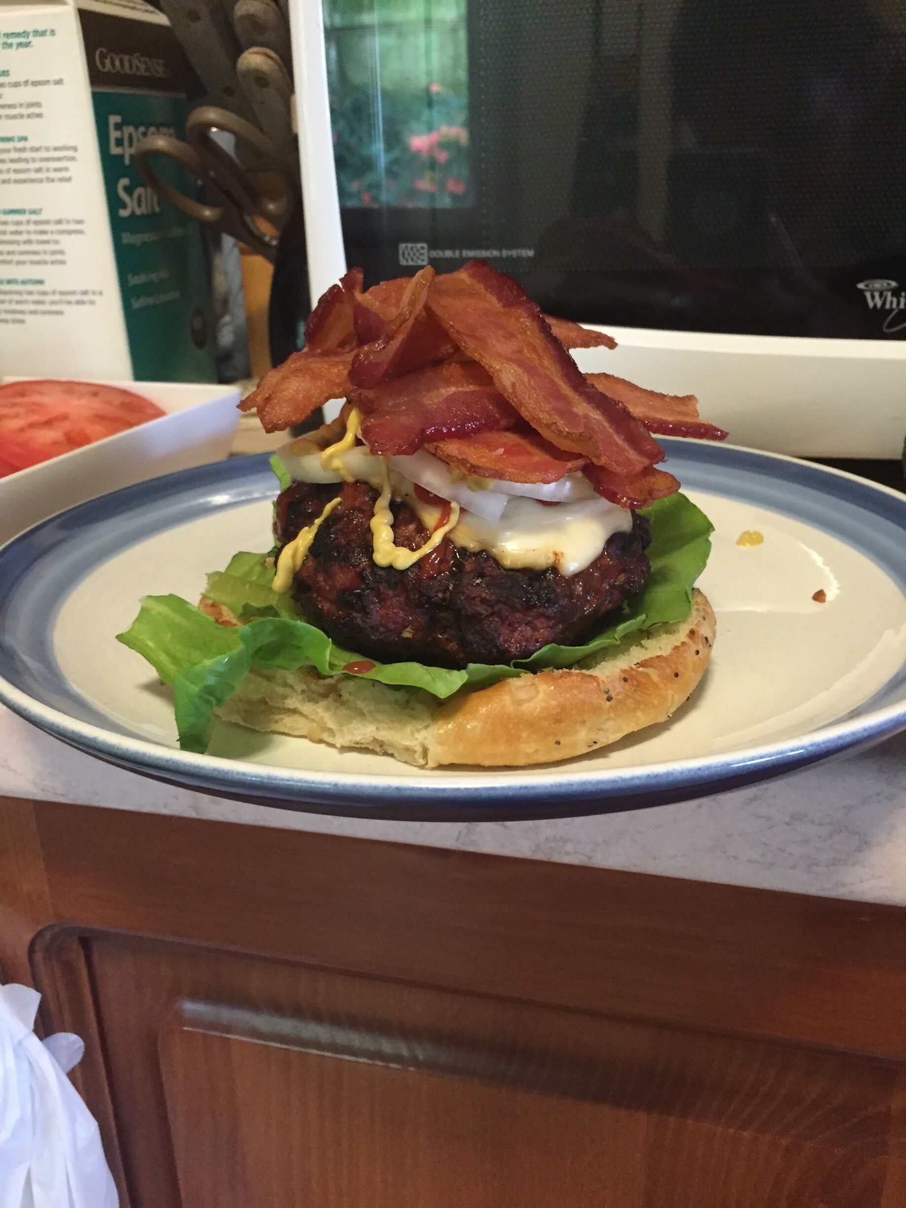 Onion roll with lettuce, burger with different kinds of seasonings and provolone cheese in the middle topped with more provolone cheese,  jalapeño ketchup, German mustard, onions and a heaping stack of bacon strips!  #Delicious #homemade 