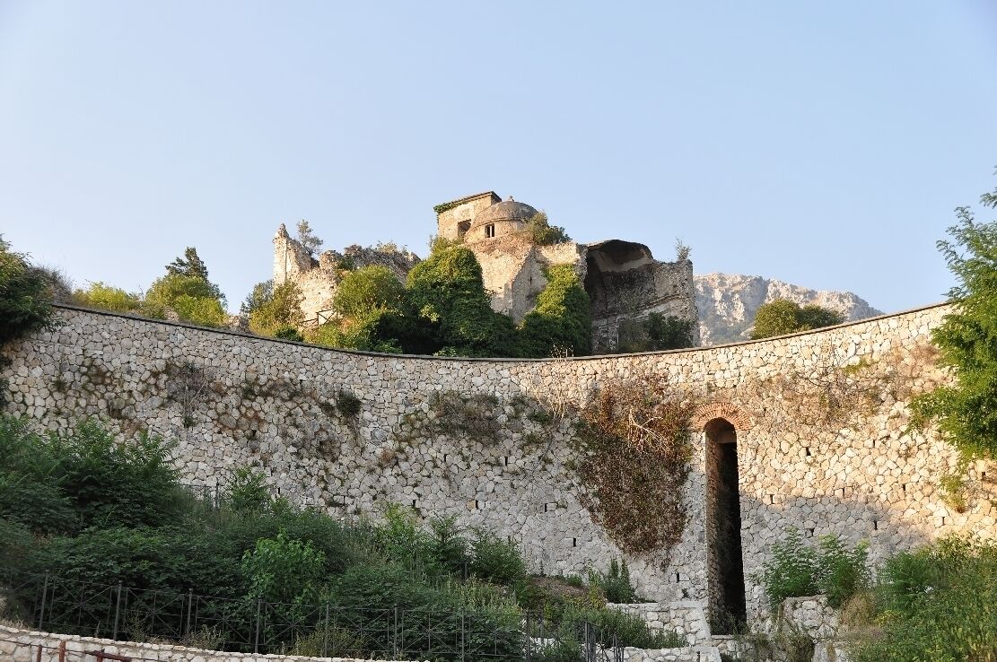 A stone wall with an arched entrance and a castle on a hill.