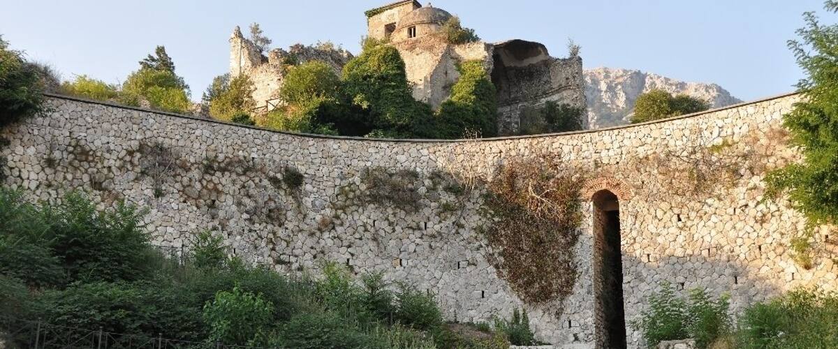 A stone wall with an arched entrance and a castle on a hill.