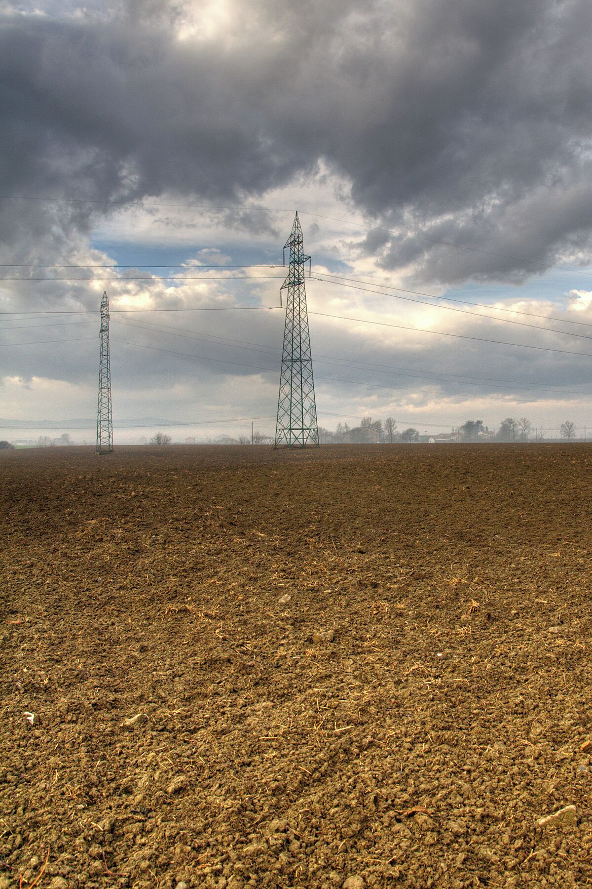 A vast, plowed field with two tall electrical transmission towers under a cloudy sky.