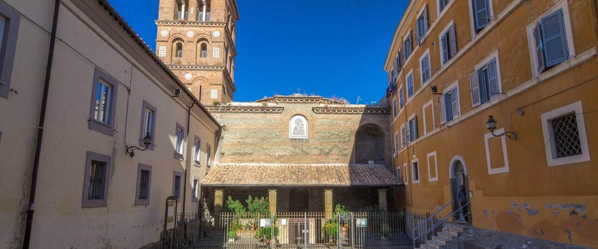 A courtyard with a church featuring a bell tower, surrounded by historic buildings.