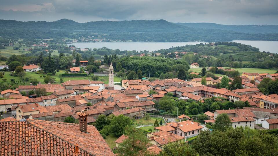 A town with red-tiled roofs, a prominent tower, and a lake in the background.
