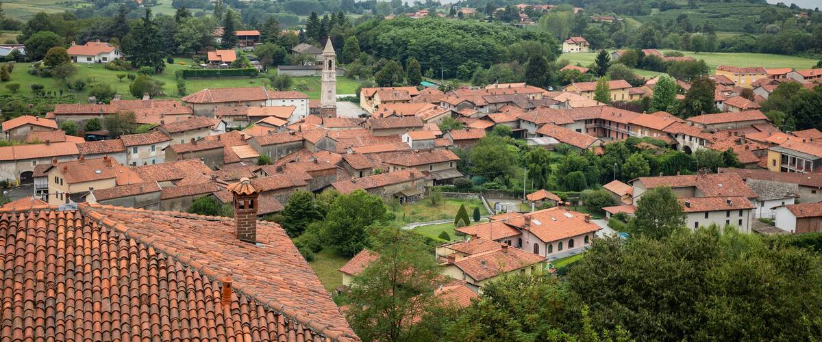 A town with red-tiled roofs, a prominent tower, and a lake in the background.