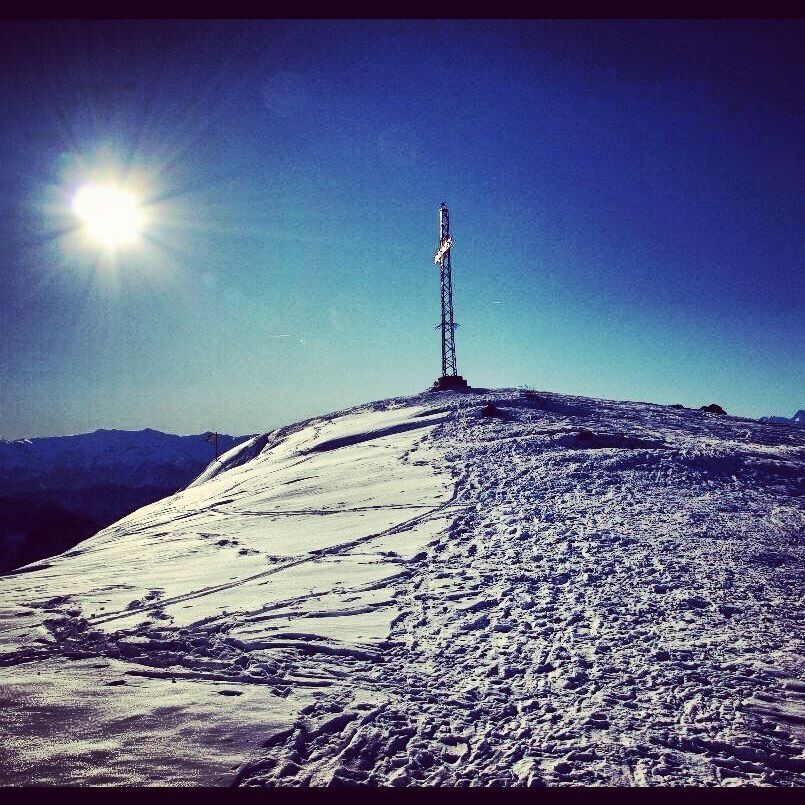 A snow-covered mountain with a tall communication tower and a clear blue sky.