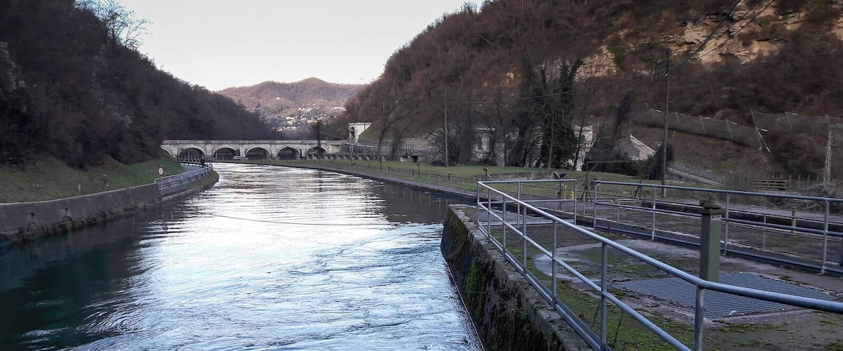 A canal with a bridge in the background, surrounded by hills and trees.