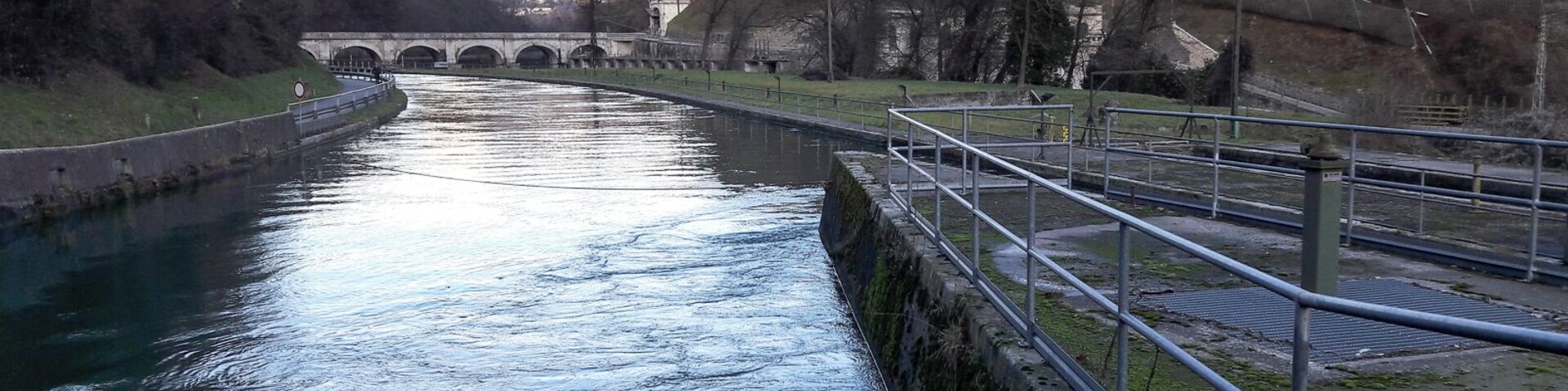 A canal with a bridge in the background, surrounded by hills and trees.