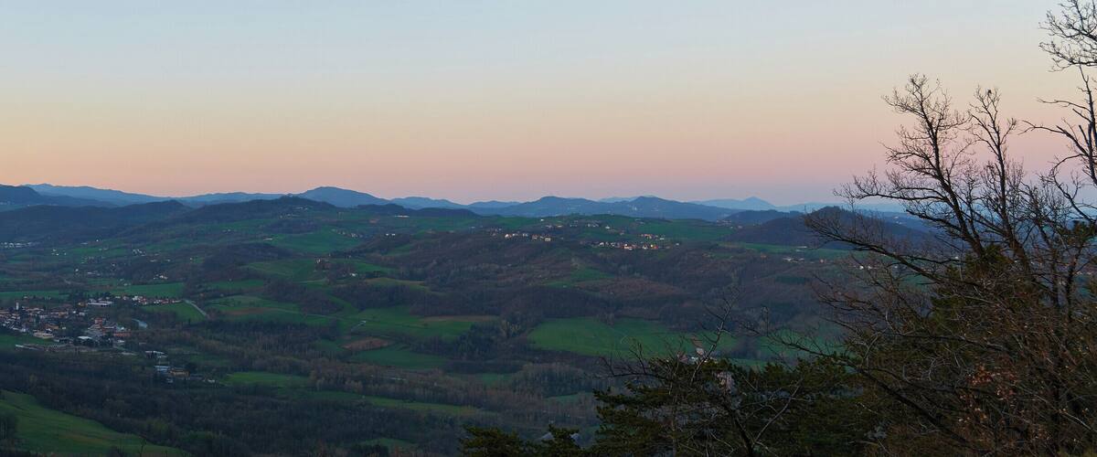 A valley with rolling hills, a small town, and distant mountains under a twilight sky.