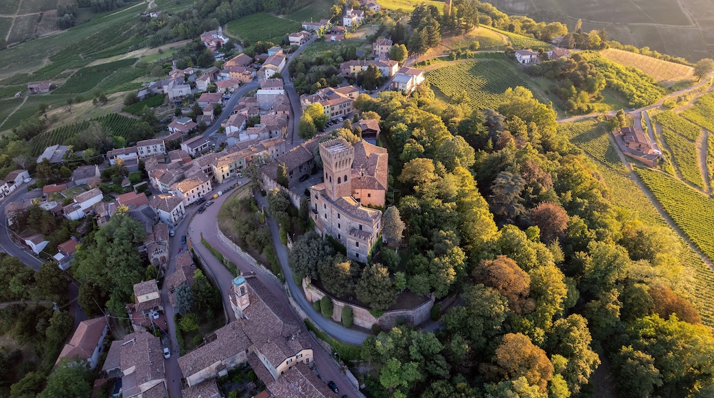 Vista aérea de un pueblo histórico con viñedos en terrazas, caminos sinuosos y una imponente construcción tipo castillo.
