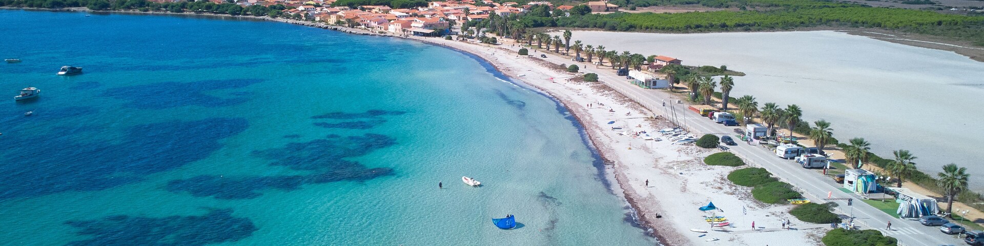 Un pueblo costero con una playa, aguas azules cristalinas y un paisaje montañoso al fondo.