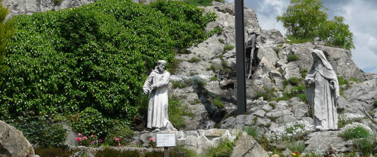 A stone cross, two statues, and a castle in the background.