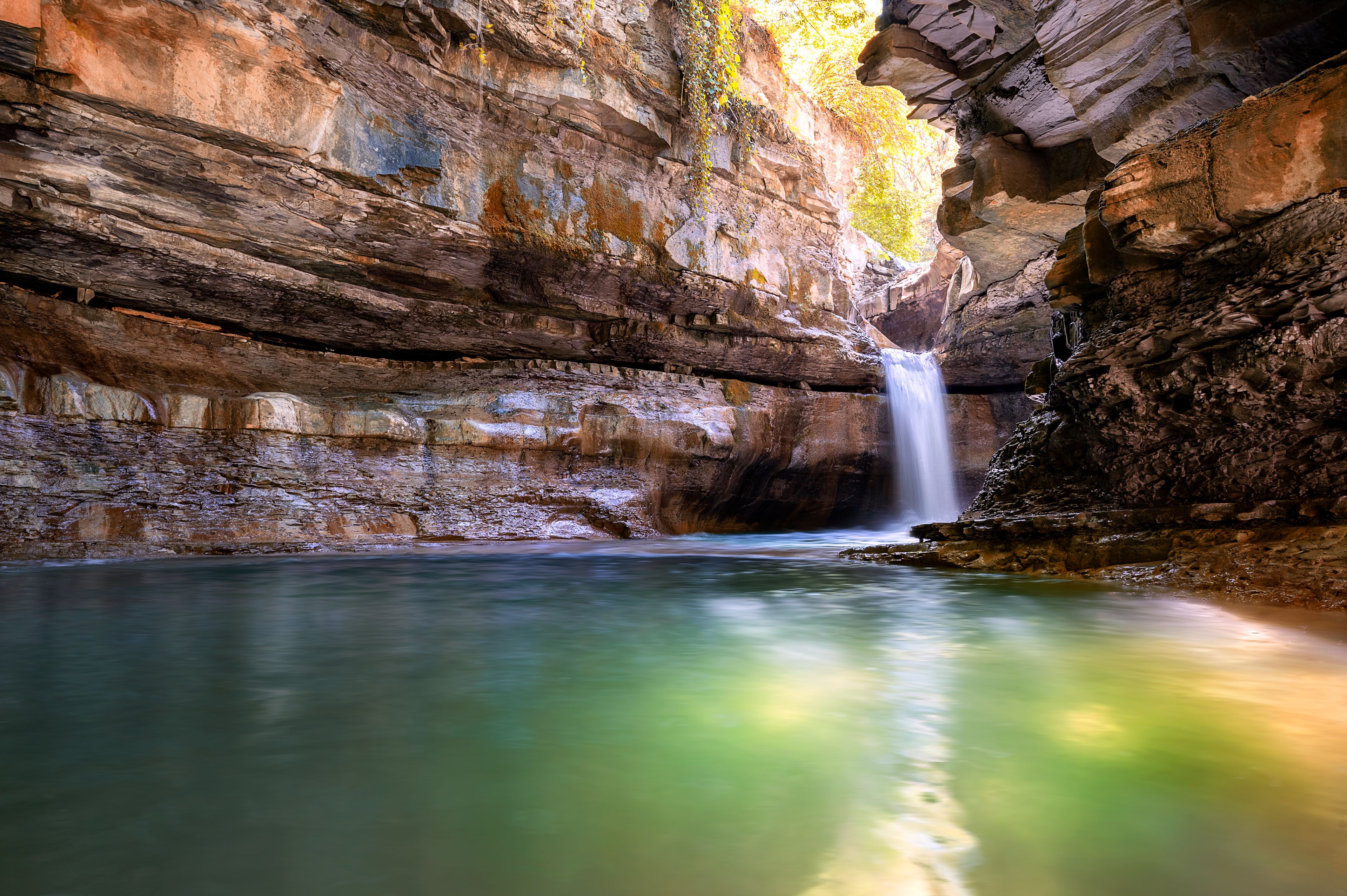 Ein Wasserfall in einer felsigen Höhle mit klarem Wasser.