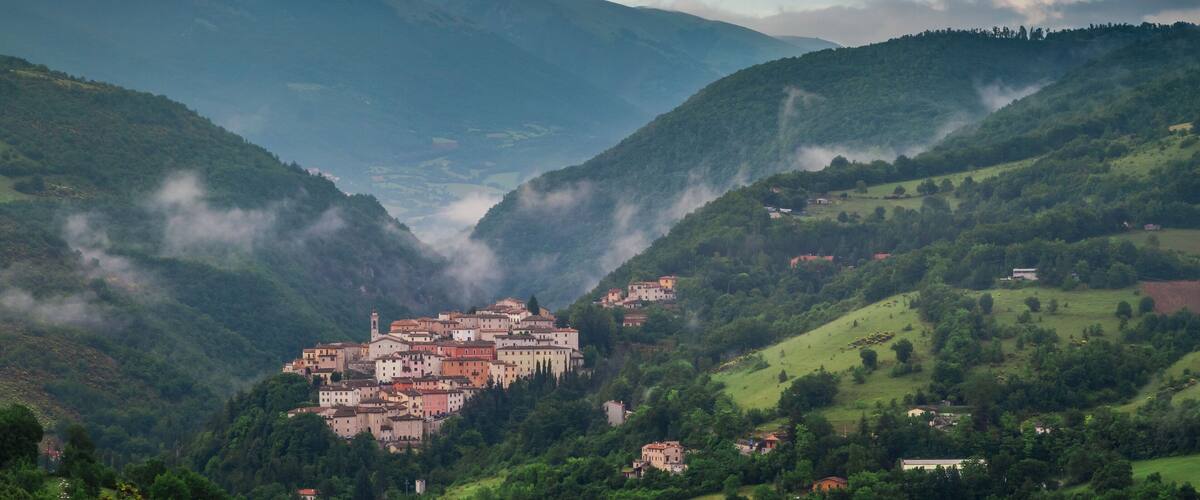 A valley with a town nestled among green hills and mountains.