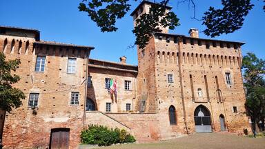 Un bâtiment historique en briques, doté d’une tour, de fenêtres en arc de cercle et d’un drapeau.