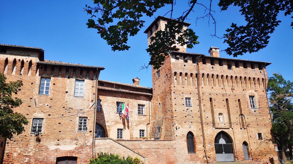A historic brick building with a tower, arched windows, and a flag.