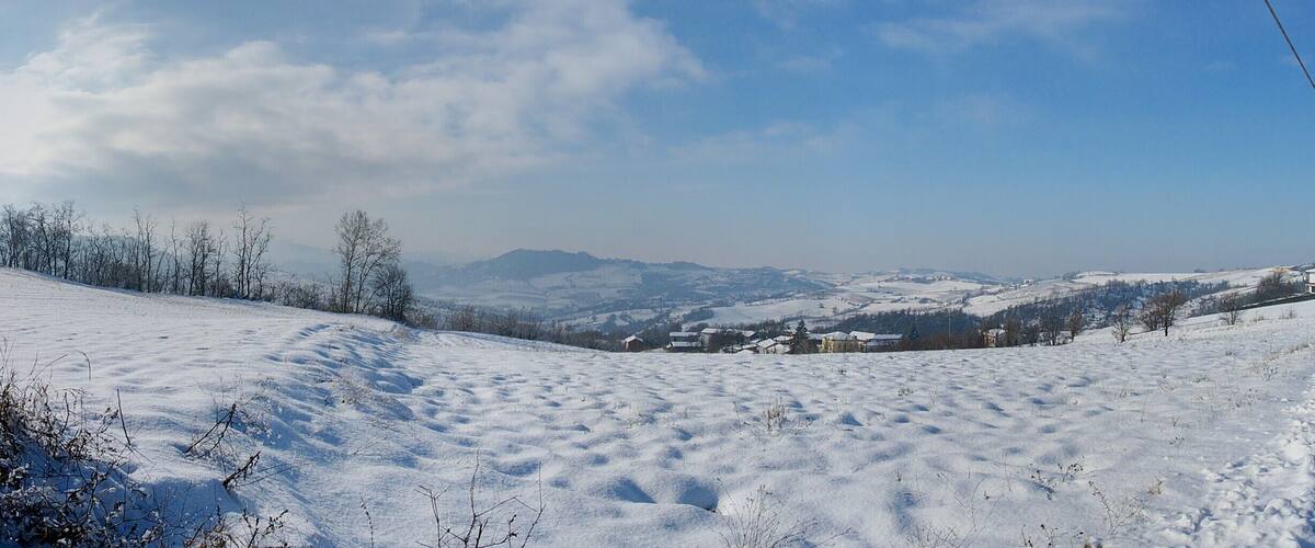 A snow-covered landscape with a road, distant houses, and mountains under a clear sky.