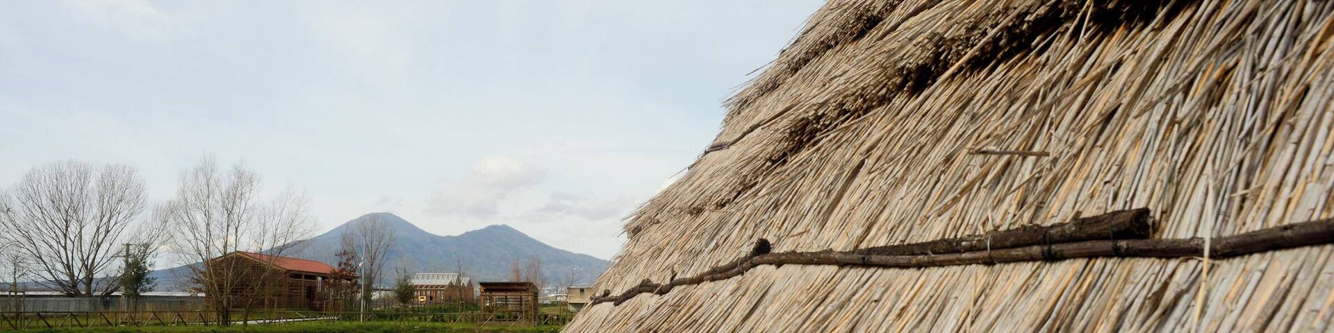 Parco archeologico del sito archeo-fluviale di Longola. Capanne del villaggio preistorico. Sullo sfondo, il Somma-Vesuvio.