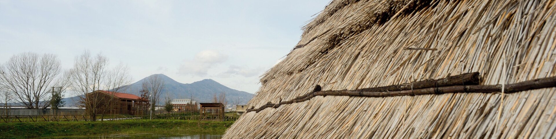 Parco archeologico del sito archeo-fluviale di Longola. Capanne del villaggio preistorico. Sullo sfondo, il Somma-Vesuvio.