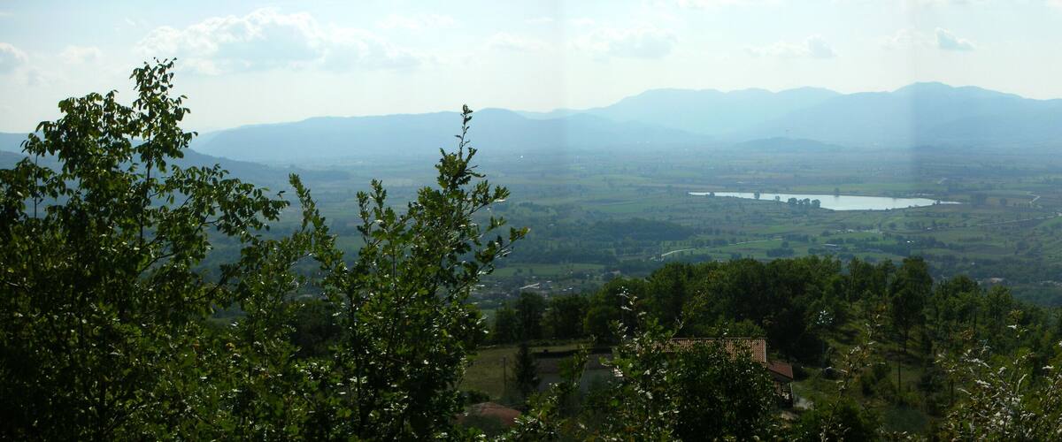 A valley with a lake, surrounded by mountains and dense greenery.