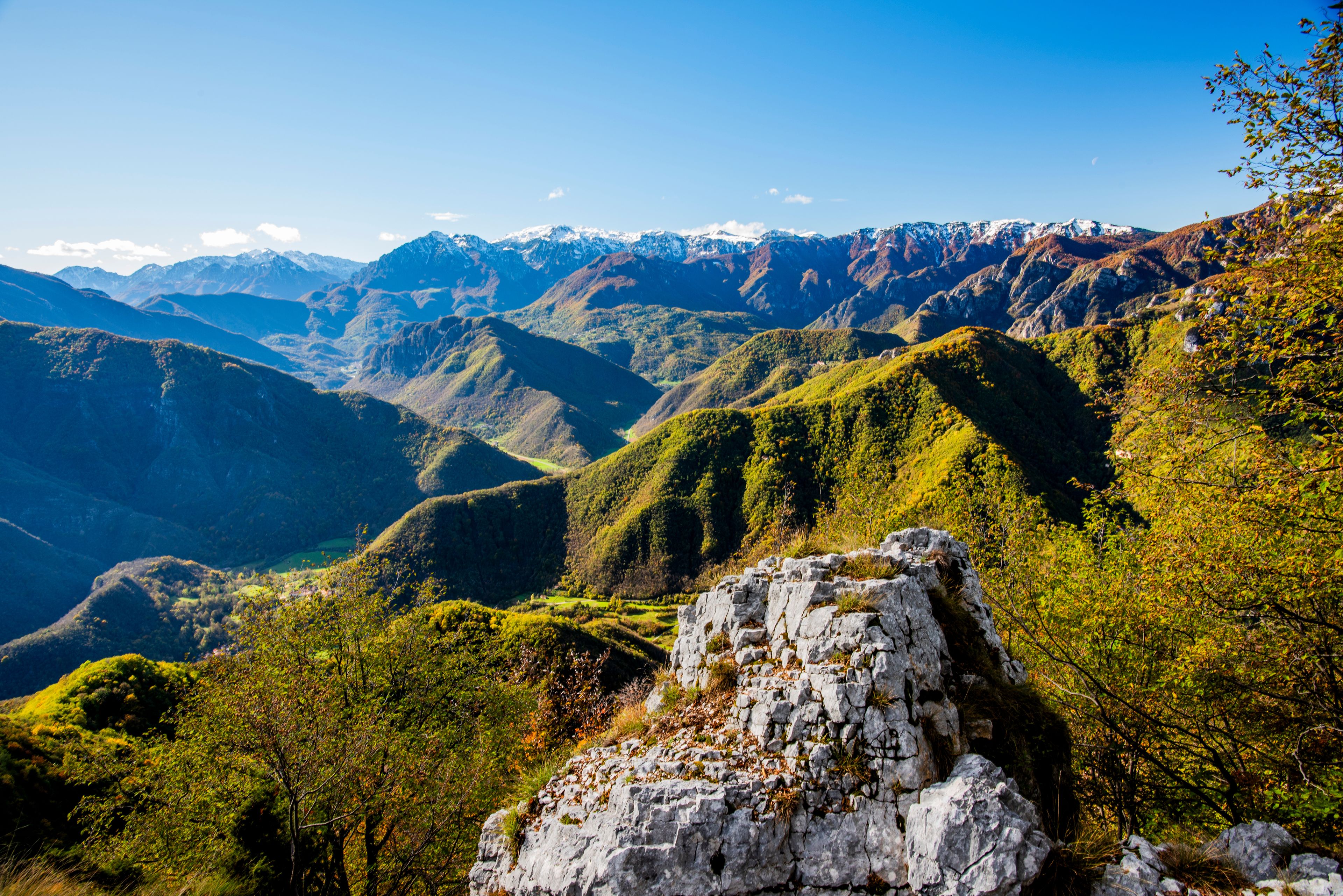 A mountainous landscape with a prominent rocky outcrop in the foreground and a valley with dense vegetation.