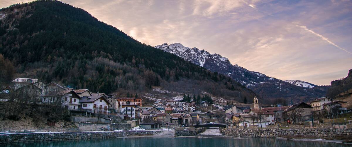 A lakeside village with houses, a church, and snow-capped mountains in the background.
