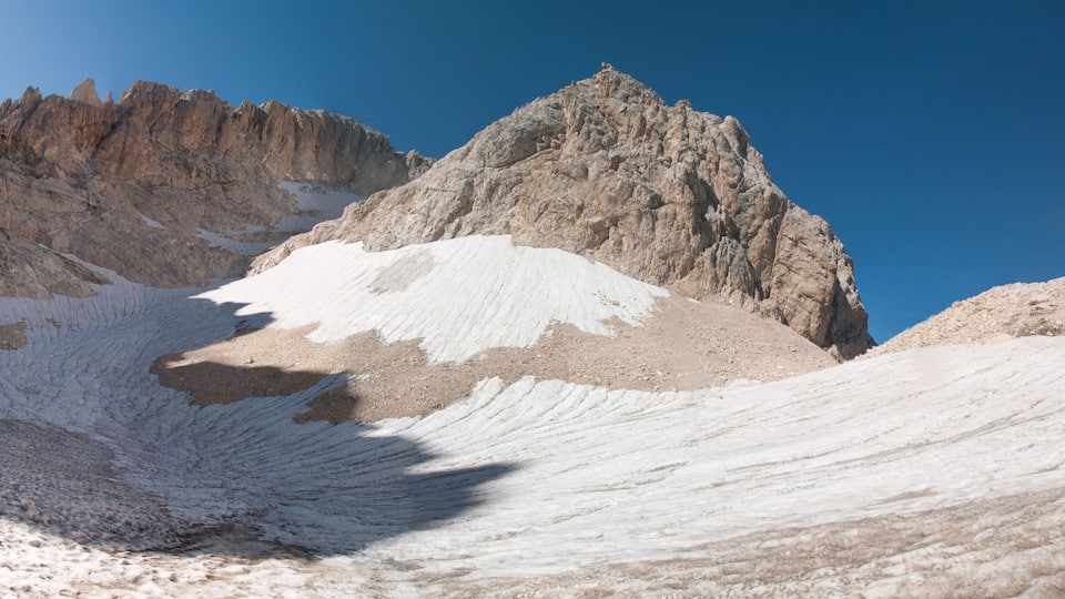 A snow-covered mountain with a rocky peak and a person standing on the snow.