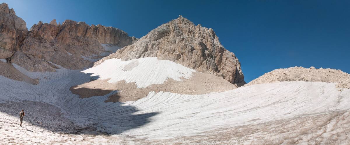 A snow-covered mountain with a rocky peak and a person standing on the snow.