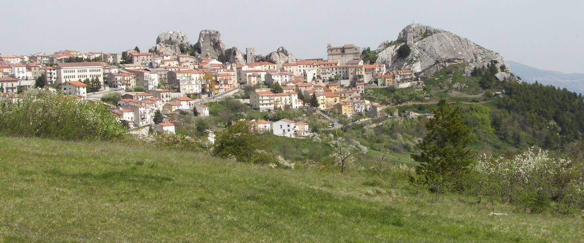 A town with buildings on a hillside, a prominent rock formation, and a clear sky.