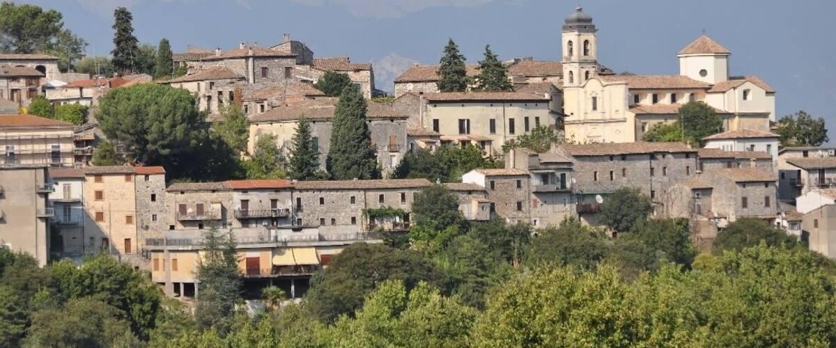 A historic town with stone buildings, a prominent church with a bell tower, and mountains in the background.