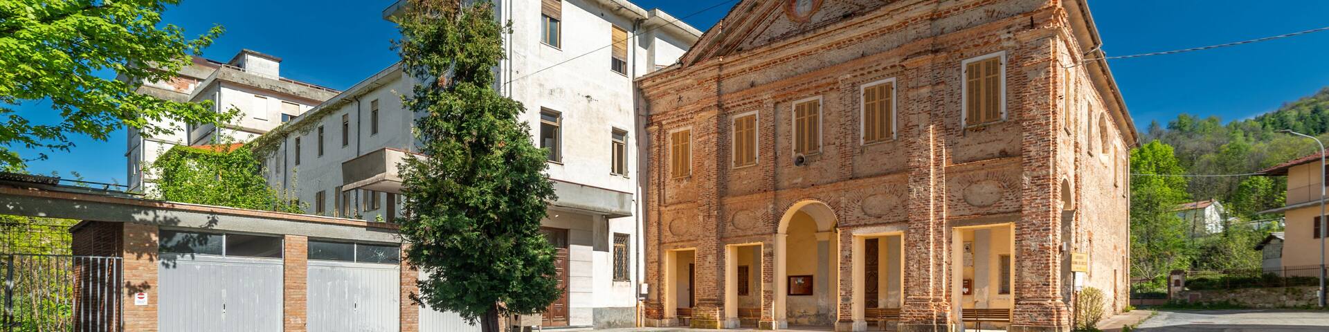 Peveragno, Cuneo, Italy - April 19, 2024: Shrine of Our Lady of the Woods or of the Borgato (13th cent.) near the abandoned building of the Salesian College from the 1960s-80s