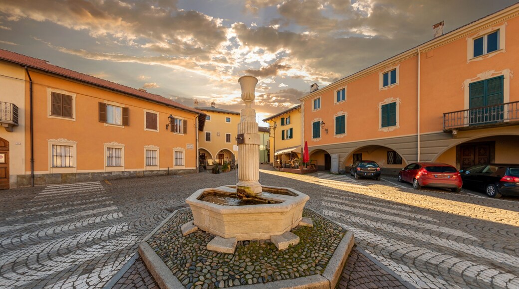 Peveragno, Cuneo, Italy - January 09; 2023: marble fountain with drinking trough on cobblestones in Piazza Santa Maria with ancient palaces decorati with arcade under cloudy sky at sunset