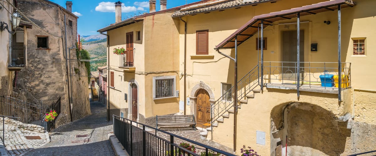 A narrow cobblestone street flanked by historic buildings with terracotta roofs and wooden shutters.