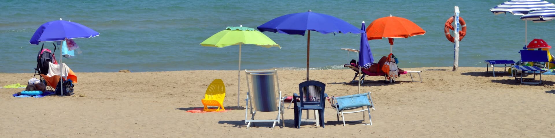 A beach with multiple colorful umbrellas, chairs, and a lifebuoy.