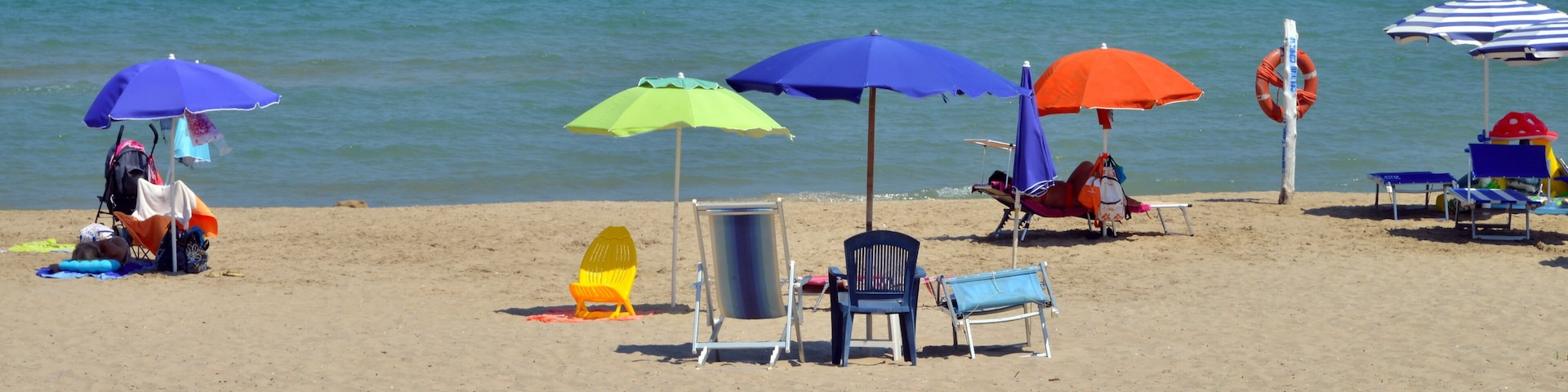 A beach with multiple colorful umbrellas, chairs, and a lifebuoy.