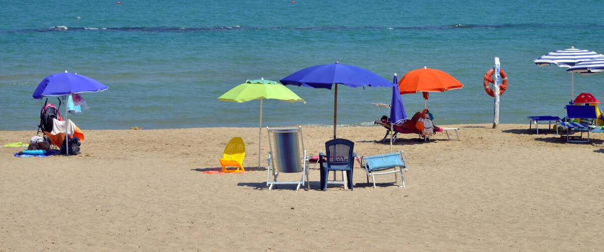 A beach with multiple colorful umbrellas, chairs, and a lifebuoy.