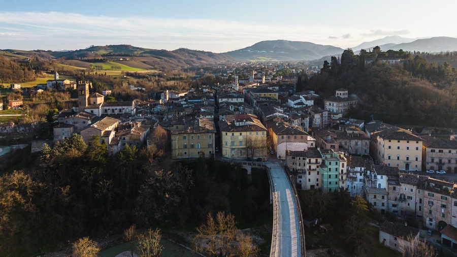 A historic town with a prominent church tower, a railway track, and rolling hills in the background.