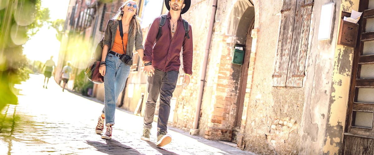Two people walking on a cobblestone street with old buildings and a wooden door.
