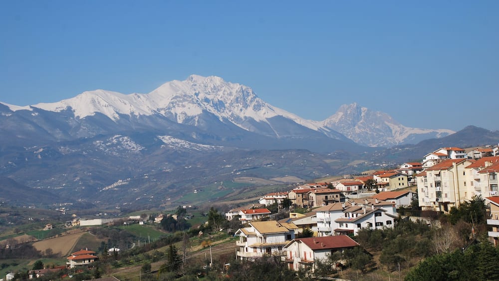 Un paysage montagneux avec des sommets enneigés et une zone résidentielle comprenant des maisons et des immeubles.