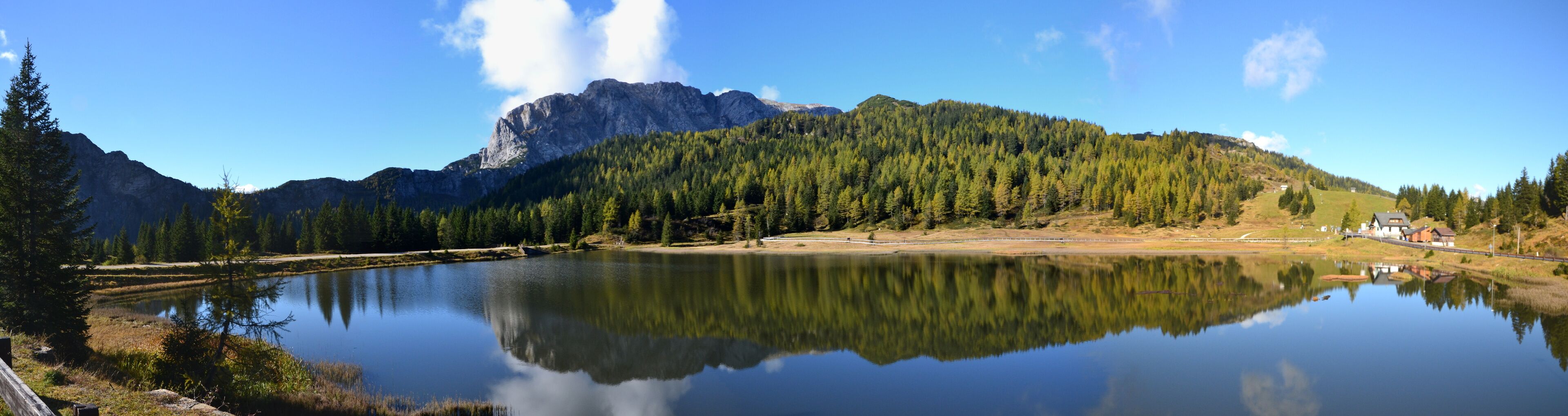A calm lake reflecting trees and mountains, with a house on the right.