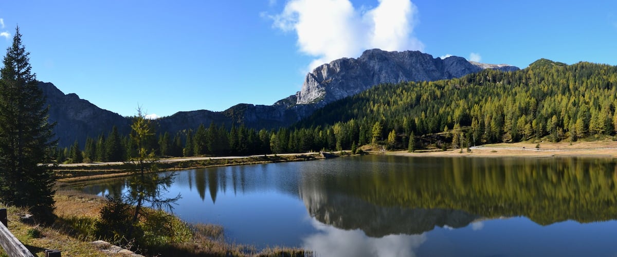 A calm lake reflecting trees and mountains, with a house on the right.