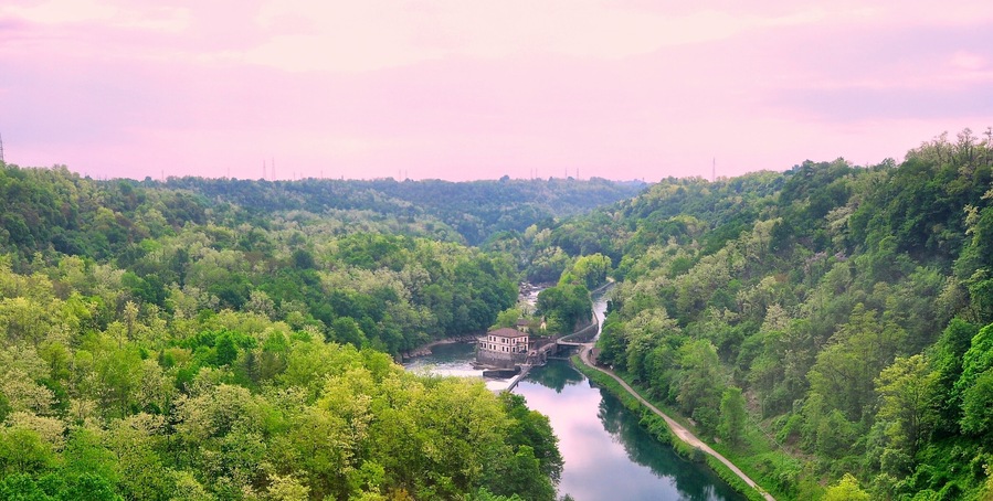 Ein Fluss schlängelt sich durch ein dicht bewaldetes Tal, nahe am Wasser steht ein kleines Gebäude.