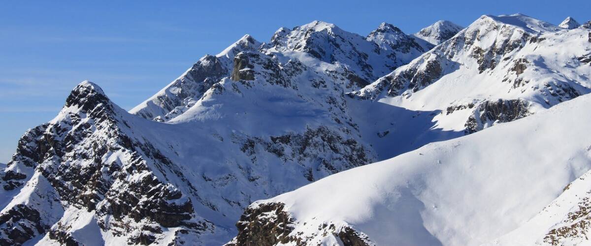 A snow-covered mountain range with sharp peaks and clear blue skies.