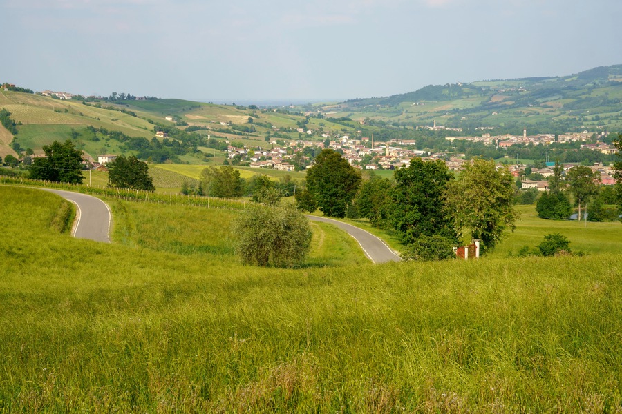 A winding road through a lush green landscape with rolling hills, a small town in the distance, and a prominent church tower.