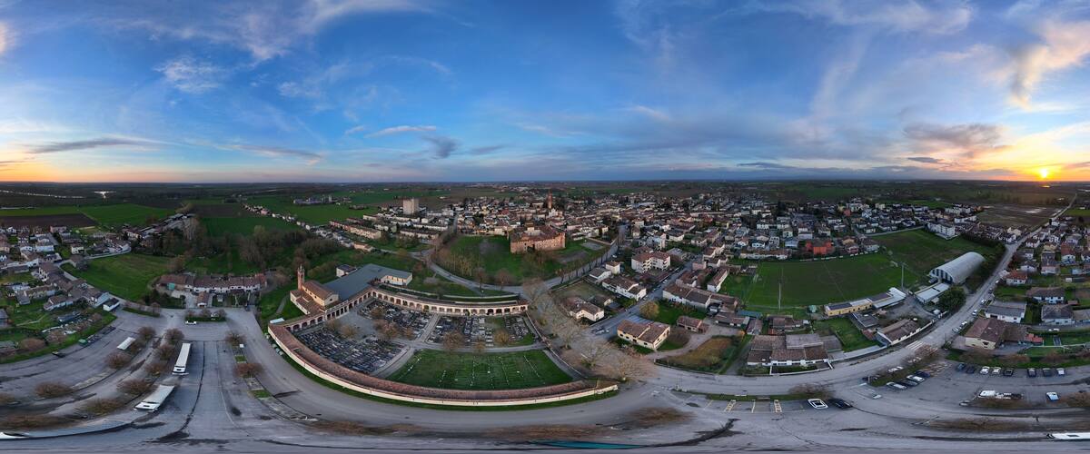 An aerial view of a town with a prominent castle-like structure, a large open field, and a winding road.