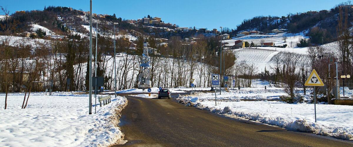A snow-covered road with a car, surrounded by hills and a clear blue sky.