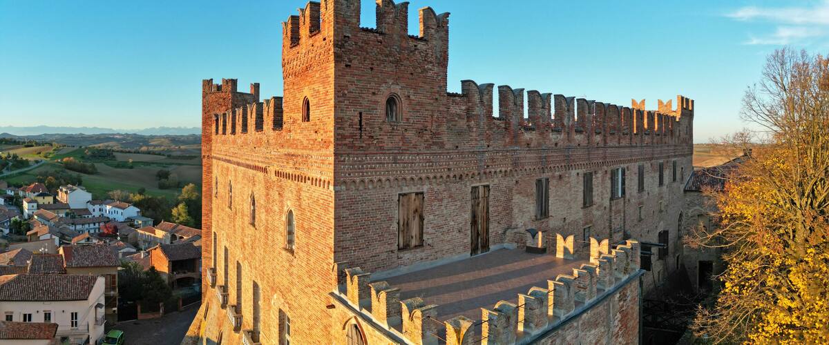 A historic brick castle with a prominent tower and battlements, surrounded by a town with traditional buildings.