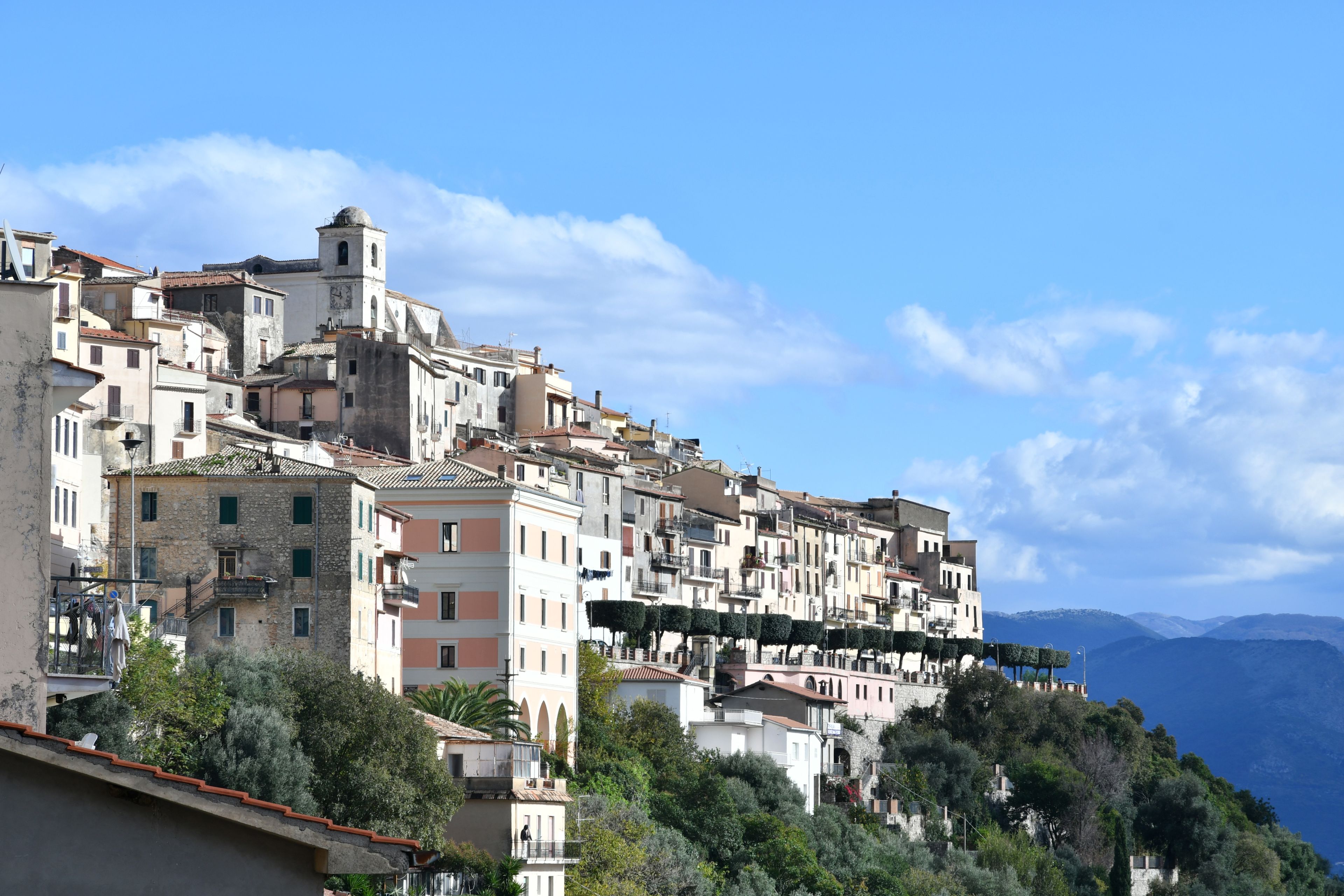 Une ville pittoresque, située sur une colline, avec des bâtiments historiques, un imposant beffroi et un paysage de montagnes en toile de fond.