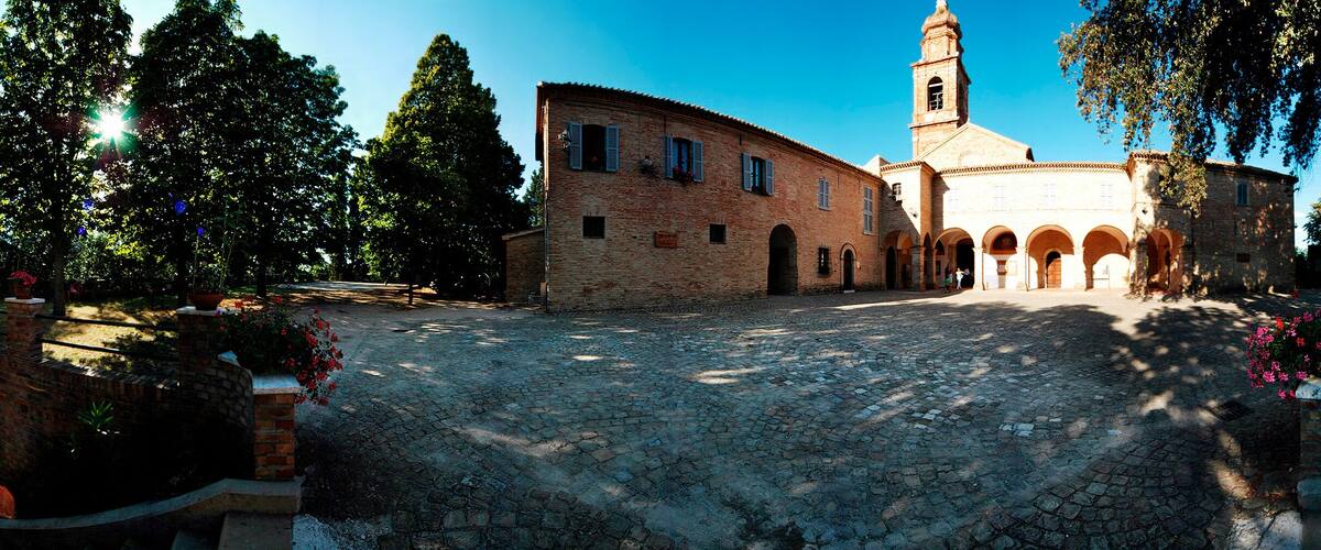 A cobblestone street leading to a historic building with a tower, surrounded by trees and flower beds.