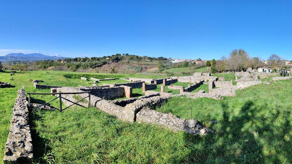 Ancient stone ruins in a grassy field with a clear blue sky.
