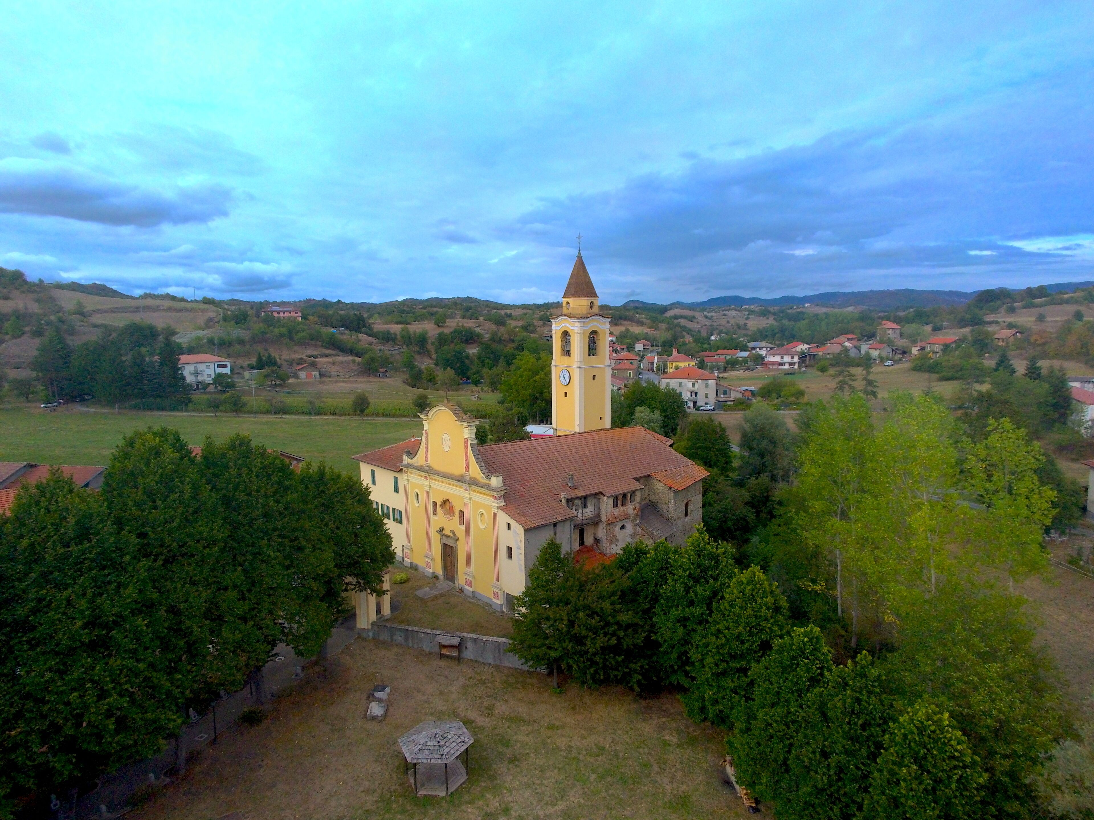 A church with a bell tower surrounded by a rural landscape with houses and trees.
